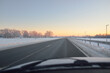 Empty highway (asphalt road) through the snow-covered forest and fields, rural area. Sunrise, snow drifts. Europe. Nature, christmas vacations, remote places, winter tires, dangerous driving concept
