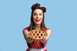 © Prostock-studio - Positive pin up woman in retro style dress holding yummy homemade pie on blue studio background