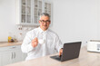 © Prostock-studio - Time for morning coffee. Mature businessman working on laptop computer and drinking hot beverage, sitting in kitchen