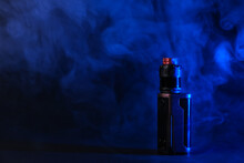 Electronic Vaping Device Mod, Atomizer Stands In Vape Smoke And Vapor Illuminated By Blue Light.