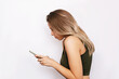 © Марина Демешко - A young blonde woman with a hunched back looks at the mobile phone screen isolated on a white background. Incorrect back position, curvature of posture, spine. Dependence on gadgets