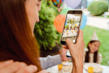 Wall Mural - White parents taking photo on cellphones during birthday party