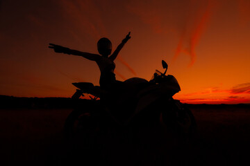 Wall Mural - silhouette of a biker woman wearing safety helmet with open arms on her motorcycle at sunset