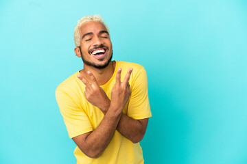 Wall Mural - Young Colombian handsome man isolated on blue background smiling and showing victory sign