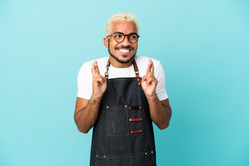 Poster - Restaurant Colombian waiter man isolated on blue background with fingers crossing