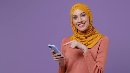 Wall Mural - Young arabian asian muslim woman in abaya hijab yellow clothes hold use mobile cell phone browsing swipe send sms doing online shopping isolated on plain pastel light violet background studio portrait