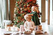 Siblings Children Boy And Little Girl With Blond Hair And Blue Eyes In Beautiful Clothes Are Standing In Living Room Near Christmas Tree With White Small Rabbits For Family Celebration Of Christmas An
