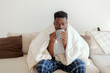 © Jelena Stanojkovic - Shot of a man having a warm drink while recovering from an illness on the sofa at home. A young man that has caught a cold is at home holding a mug of hot tea, feeling bad.