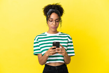 Canvas Print - Young african american woman isolated on yellow background using mobile phone