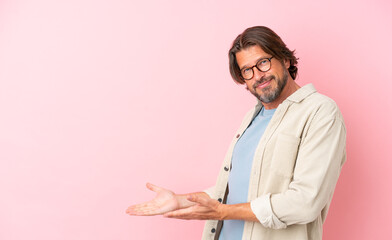 Wall Mural - Senior dutch man isolated on pink background extending hands to the side for inviting to come