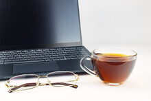Laptop, Glass Cup With Tea, Glasses With Gold Rim On A White Background, Close-up. 