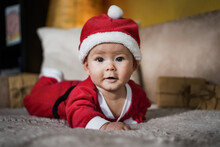 Cute Little Newborn Baby In Christmas Outfit With Santa Claus Hat Crawling On A Couch In A Cozy Bright Living Room 
