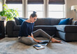 © Cavan Images - Woman sitting on floor in living room working on computer.