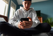 © Cavan Images - Low angle of teen boy in white sweater on smartphone in bedroom.