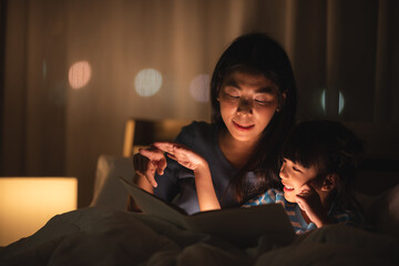 Wall Mural - young Asian mother and little daughter girl on bed, cozy love sleepy at childhood home, at night