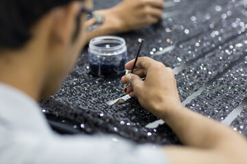 Handicraft tailor embroidering black sequins beads onto tulle. Making a dress.