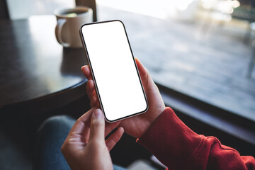 Mockup image of a woman holding mobile phone with blank desktop screen in cafe