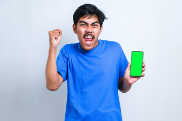 Young asian man using smartphone screaming proud and celebrating victory and success very excited, cheering emotion