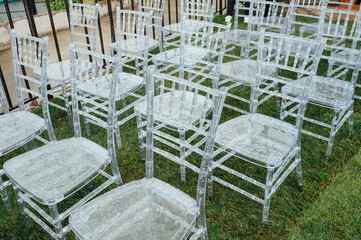 White glass chairs stand on the green grass. Round arch for a wedding ceremony In the background . Raining day