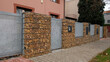 Gabion retaining wall - brown stones in gabion metallic baskets kept by retaining wall. Modern privacy fence of natural stones and galvanized steel grid surrounding residential House. 