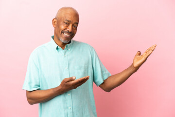 Wall Mural - Cuban senior isolated on pink background extending hands to the side for inviting to come