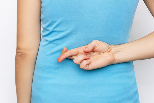 Cropped shot of a young woman in a blue t-shirt crossing her fingers behind her back isolated on a white background. Deception, lies, cheat