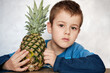 Cute Caucasian 7 year old boy with brown eyes holding a pineapple looking at the camera.