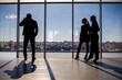 © DSMT - Two women and a man in the office enjoy the view of the city from the window of a skyscraper and talk while standing by the large window in the office