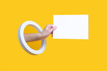 Female hand holding a blank sheet in a round hole on a yellow background.