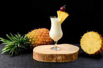 two glasses with pina colada cocktail, a whole pineapple next to the drinks, isolated on black background