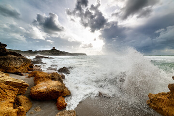 Wall Mural - Wave crashing against the rocky shore at sunset