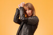 Portrait of an attractive blonde woman wearing a studded leather jacket against a yellow background