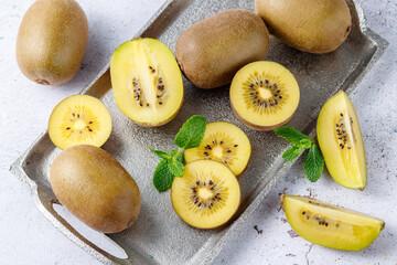 Ripe raw kiwi gold whole and slices on vintage silver metalic tray with mint leaves