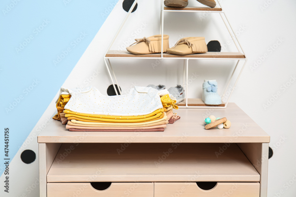Stand-up table with baby clothes near color wall