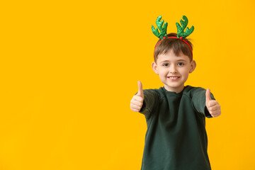 Sticker - Funny little boy with reindeer horns showing thumb-up on color background