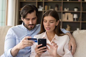 Wall Mural - Focused millennial couple of consumers using banking app on mobile phone, credit card for online payment, transaction, transfer, money order, shopping on internet, paying bills, entering data