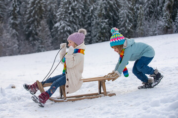 Wall Mural - Cute children boy and girl playing on a winter walk in nature. Winter knitted kids clothes. Cold weather. Happy little kids wearing knitted hat, scarf and sweater. Cold and snowy winter mountains.