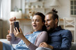 © fizkes - Excited surprised millennial dating couple getting unexpected news on smartphone, reading text message, staring at screen together with shocked amazed faces. Happy girl and guy using mobile phone