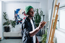 Inspired Happy Black Man Painting On An Easel Inside Of His Apartment