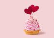Saint Valentines Day background. Cupcake or tartlet with pink meringue cream decorated with two big red hearts, love symbol, and small heart shape candies. Copy space, pink background.