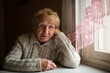 A distraught and puzzled old woman sits by the window in her house.