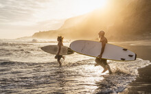 Happy Fit Friends Surfing Together On Tropical Beach At Sunset Time - People Lifestyle And Extreme Sport Concept