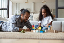 African Dad, Little 5s Beautiful Curly Haired Daughter Play Wooden Cubes Toys Sit On Warm Floor With Underfloor Heat System At Modern Home. Happy Fatherhood, Leisure, Fun, Children Development Concept