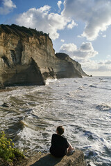 Wall Mural - Young woman sits on a stone and admires the sea and rocks. High quality photo