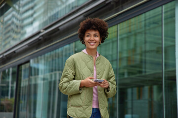 Wall Mural - positive young woman with happy smile on face uses navigation app on mobile phone enjoys travel jour