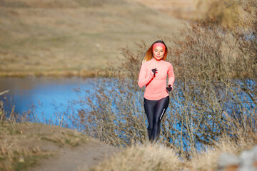 Wall Mural - Young fitness woman running in the morning in cold sunny weather. Slim jogging girl in the park