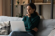 © fizkes - Pensive millennial hispanic woman sit on sofa at home work online on laptop think or make decision. Thoughtful young Latino female look at computer screen plan or solve problem. Technology concept.