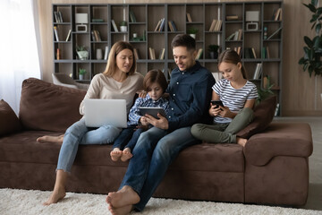 Addicted to modern technology happy bonding young couple parents and little cute children siblings using different gadgets, playing games, spending time online in social networks or shopping.