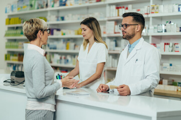 Wall Mural - Two pharmacist giving prescription medications to senior female customer in a pharmacy