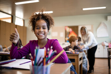 Portrait of smiling Afro American school child sitting in classroom with classmates and teacher in background.